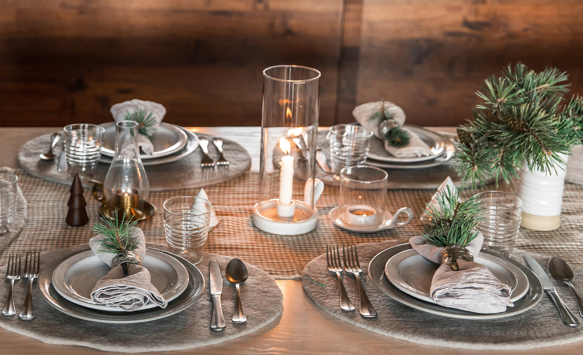 Elegant table setting with plates, silverware, candles, and decorative elements on a wooden table.